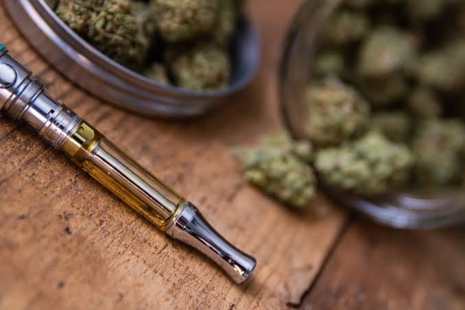 510 thread glass vape cartridge filled with golden cannabis distillate oil next to dried cannabis buds on a rustic wood surface - Weed Pen vs Vape guide by VapeFeat
