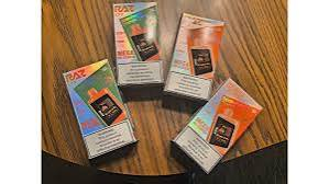 Four holographic retail packaging boxes for Raz DC25000 disposable vapes arranged on a round wooden table - Raz DC25000 unboxing and review by VapeFeat