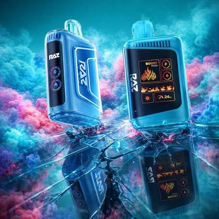 Two blue Raz DC25000 smart disposable vapes displayed on shattered reflective glass with colorful pastel smoke clouds showing side indicators and 24W Boost Mode screen - Raz Vape review by VapeFeat