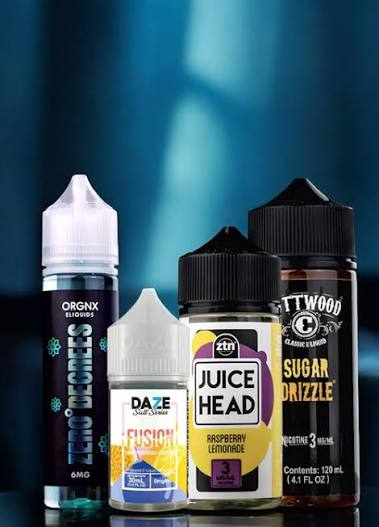 Four premium vape juice bottles including ORGNX Zero Degrees, 7 Daze Salt Series Fusion, Juice Head ZTN Raspberry Lemonade, and Cuttwood Sugar Drizzle on a reflective surface - Best E-Liquid Brands guide on VapeFeat