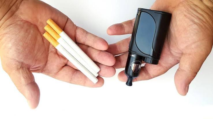 Hands holding three tobacco cigarettes in one palm and a black compact box mod vape with tank in the other on a white background - Smoking vs Vaping Comparison Guide on VapeFeat
