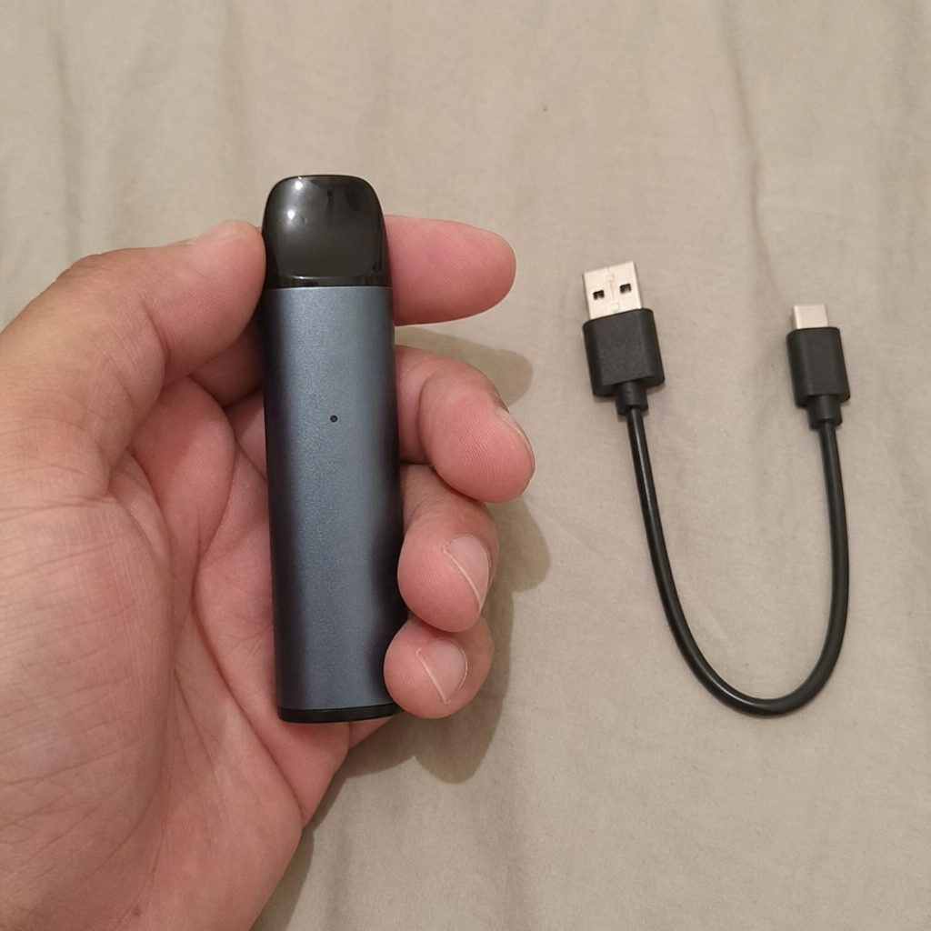 Person holding a compact grey rechargeable pod vape alongside a short black USB-C charging cable - Rechargeable Vape guide by VapeFeat