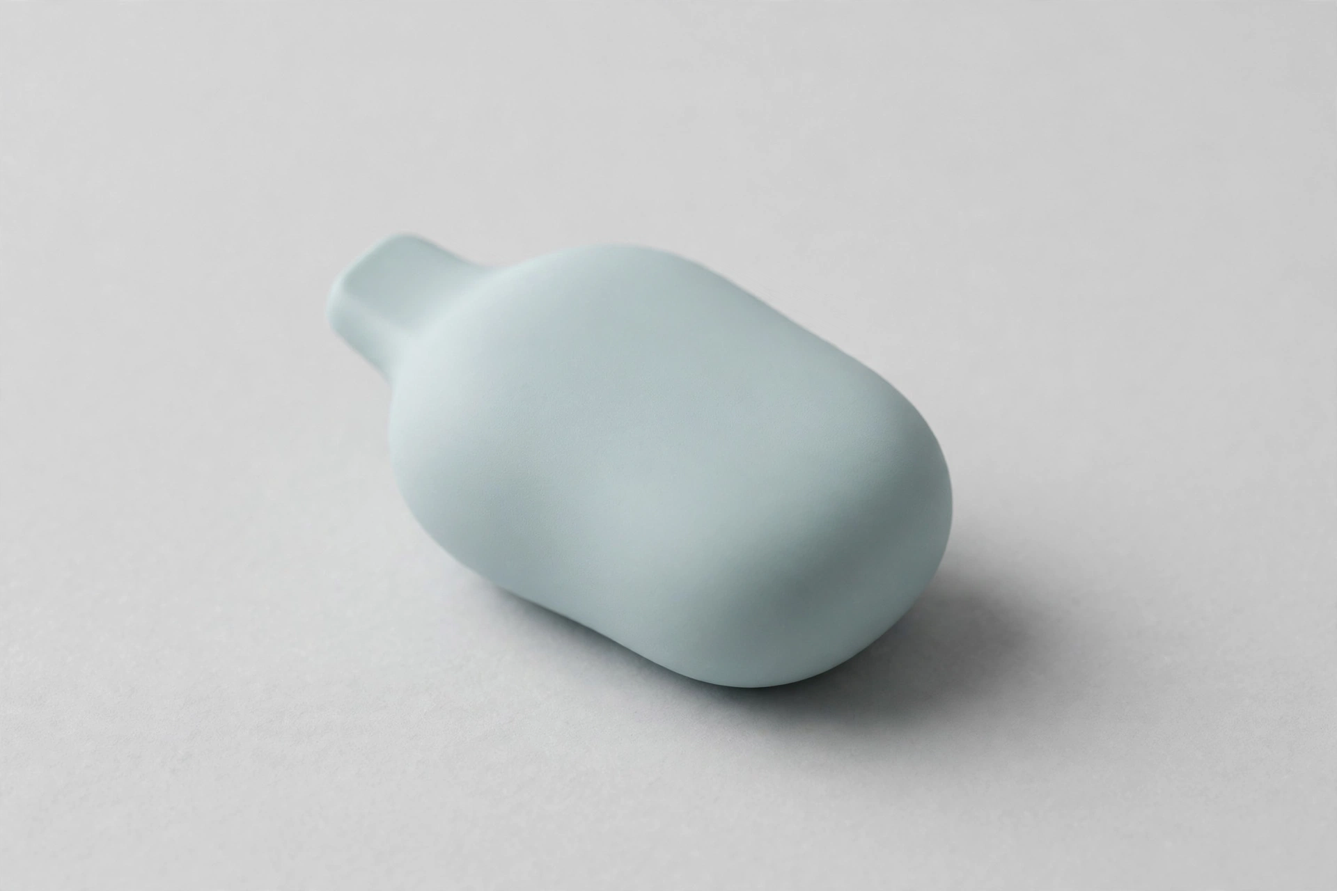 Editorial studio photo of a smooth pebble-shaped disposable vape device with a soft matte pastel finish on a light gray background